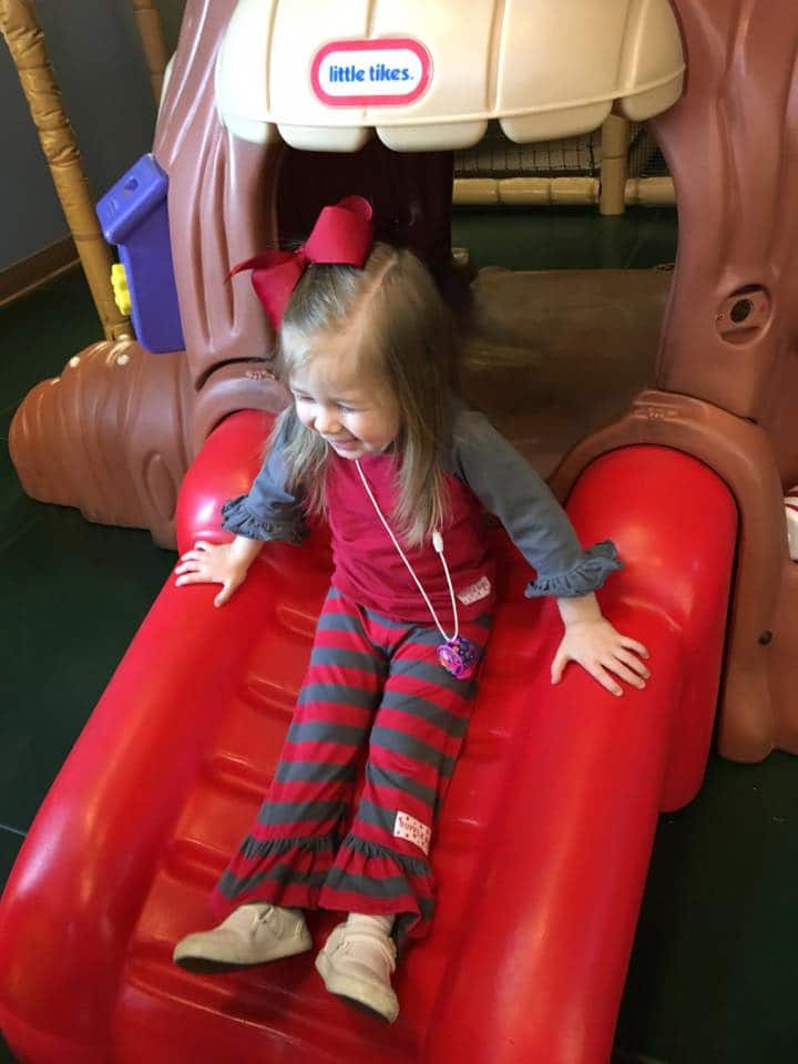 little girl sliding down slide smiling