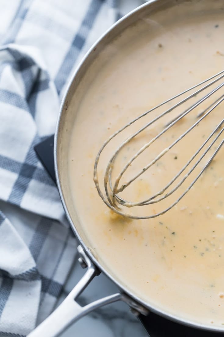 cheese cream sauce in a skillet with a whisk
