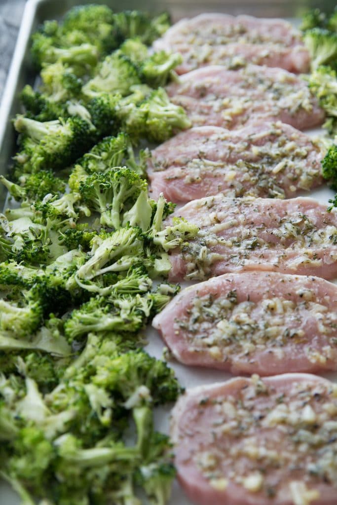 pork chops on a baking sheet with broccoli ready to go in the oven
