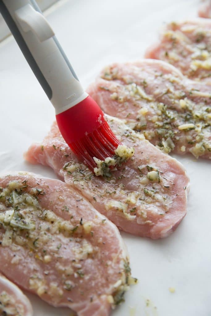 boneless thin pork chops on a sheet pan with a baster adding seasoning