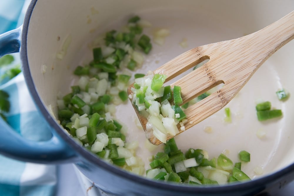 chopped peppers, onions and garlic simmering in a pot with a wooden spoon