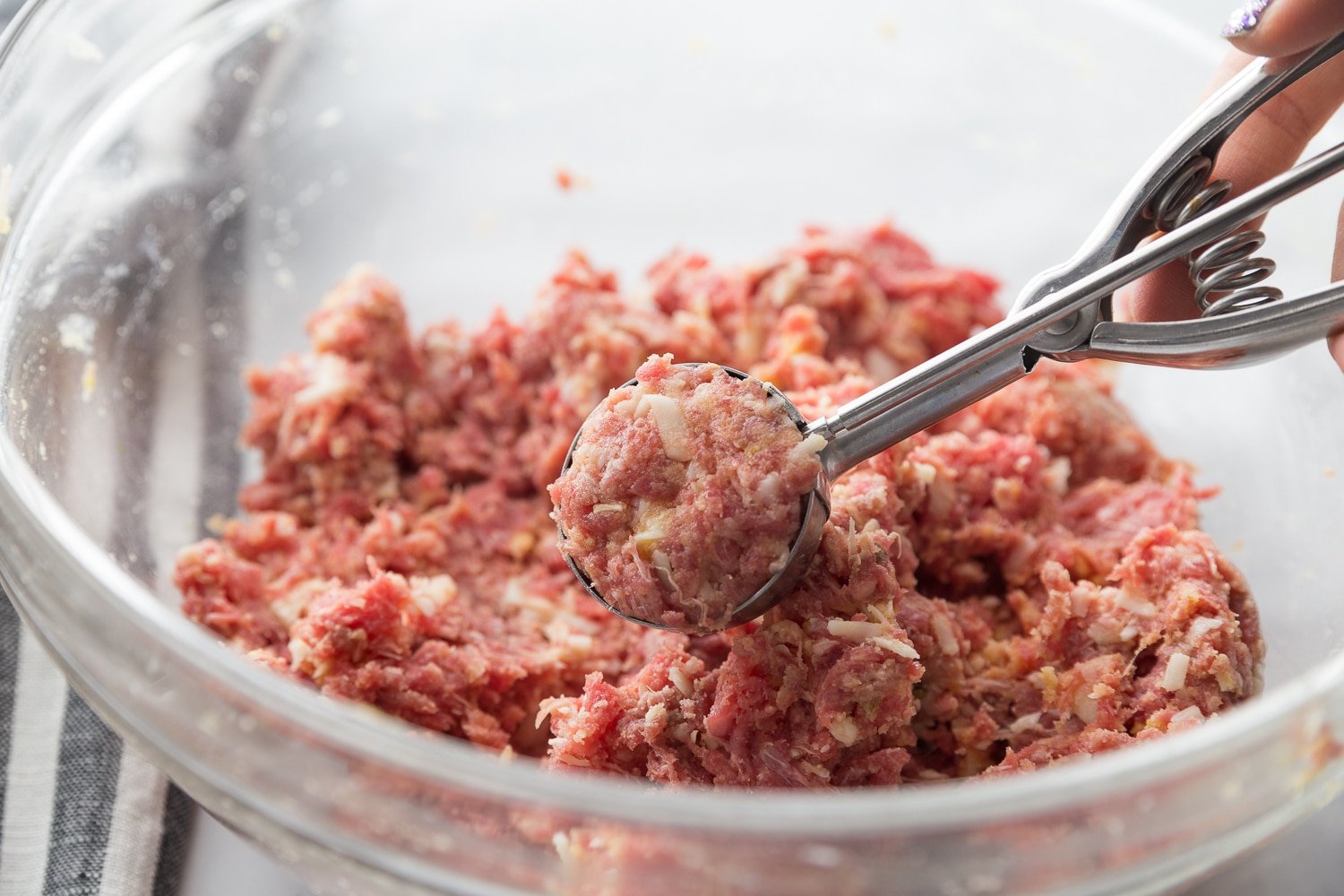 the meatball mixture being scooped out in a cookie scoop 