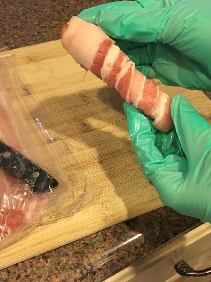 Gloved hands wrapping bacon around a cheese stick