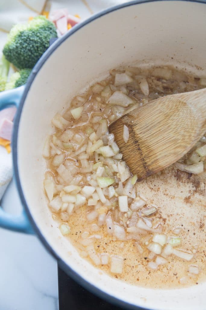 frying onions in bacon grease in a stock pot stirring with a wooden spoon