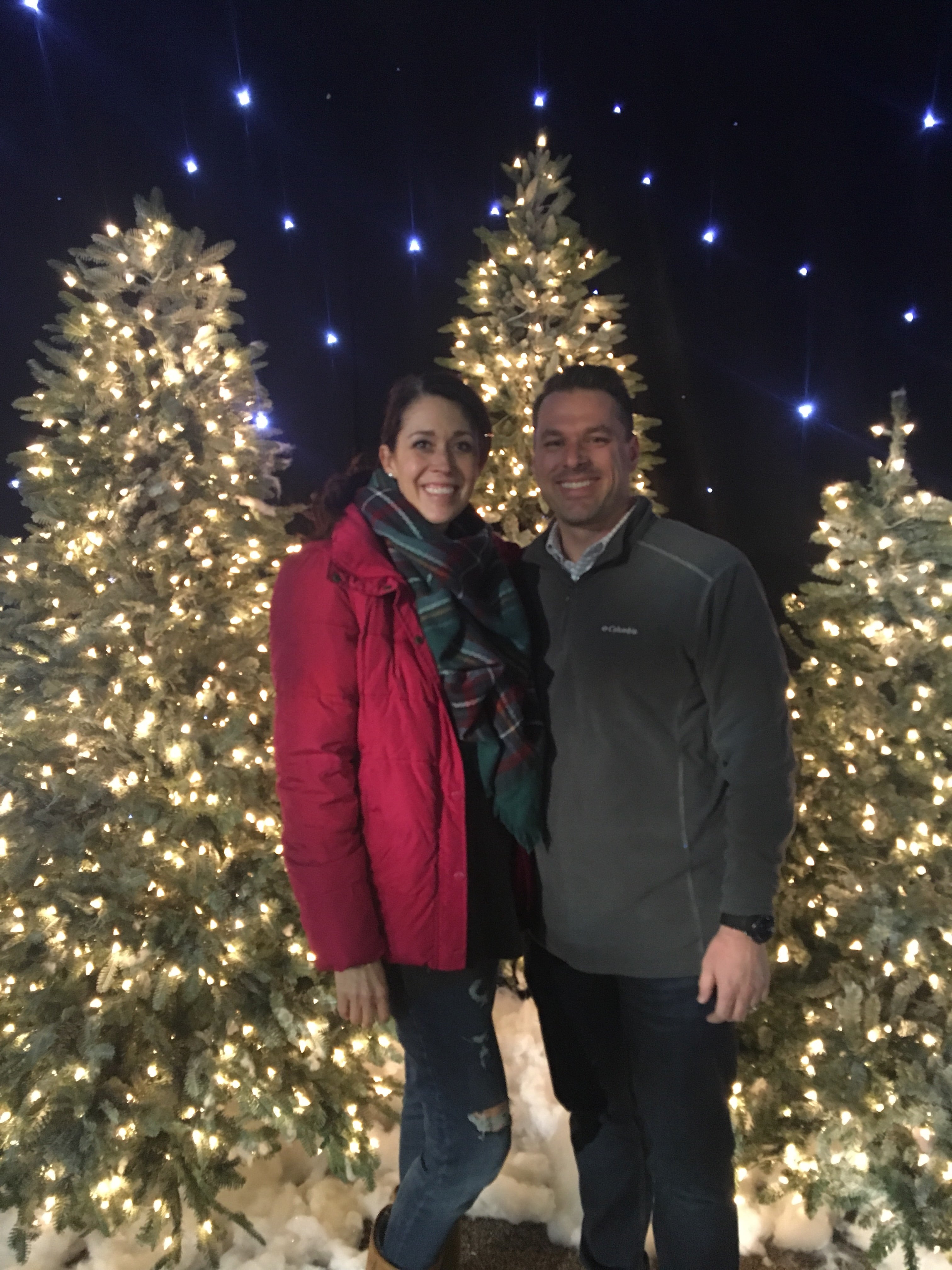 lady and man in front of lit Christmas trees
