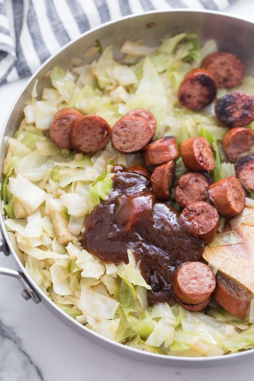adding smoked sausage to cabbage in a skillet