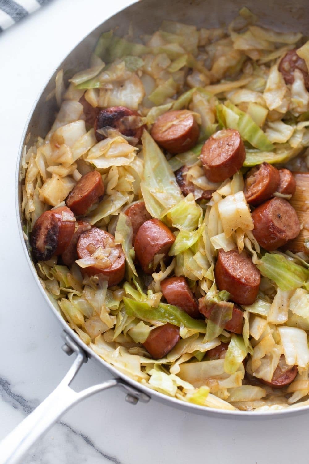 Close up photo of an easy one pan skillet meal perfect for keto and low carb diets - sliced smoked kielbasa sausage browning and caramelizing in a skillet with fresh cabbage, diced onions, garlic, and seasonings