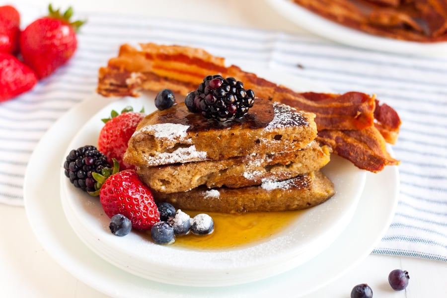 Keto french toast with bacon and berries on the side, covered with syrup and powdered sugar.