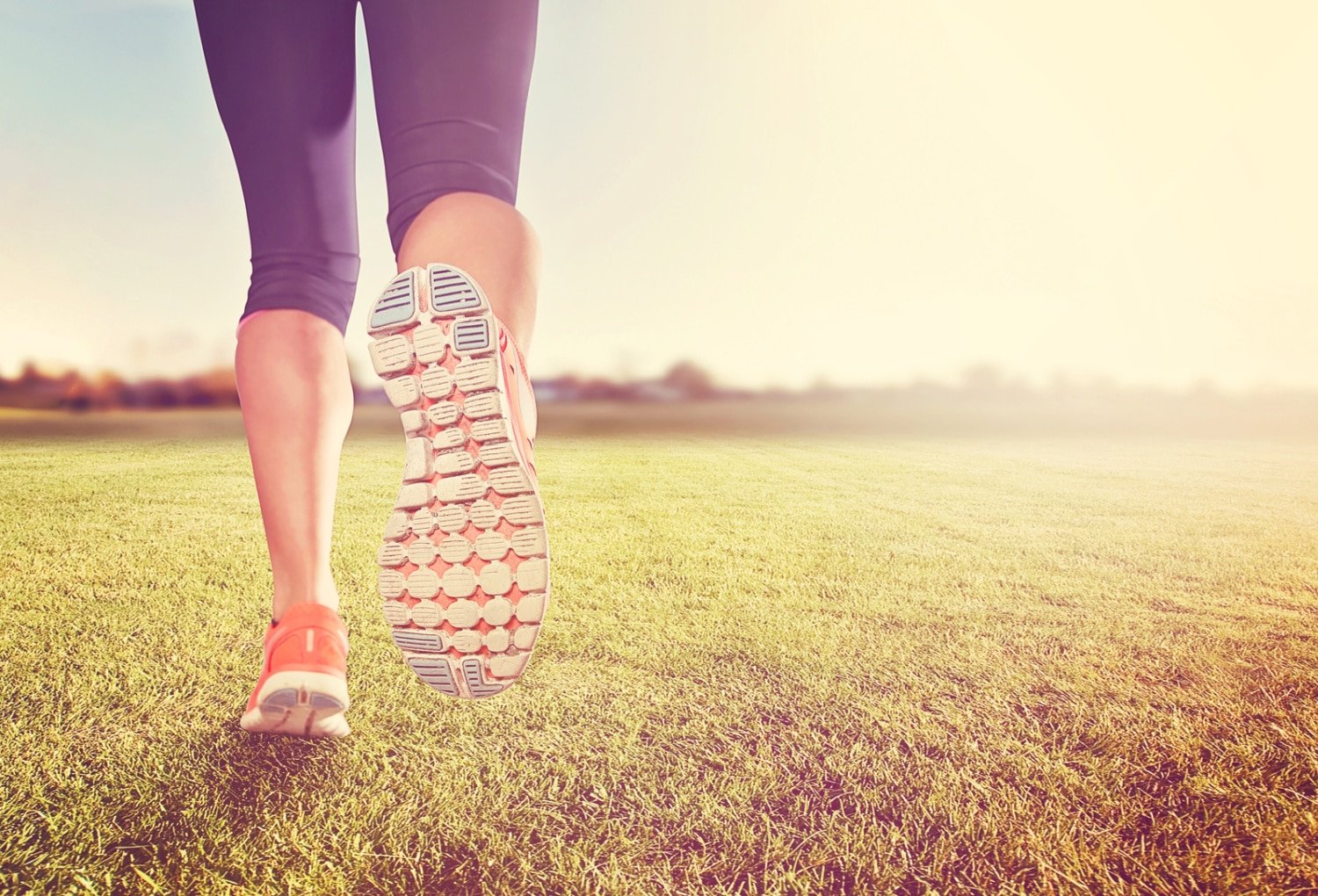 an athletic pair of legs on grass during sunrise or sunset - healthy lifestyle concept