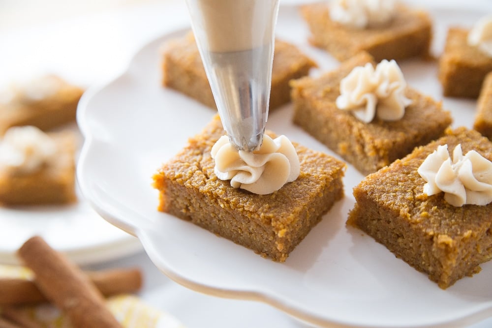 Keto Pumpkin Pie Bars on a cake dish with piping bag adding cream cheese icing to the top