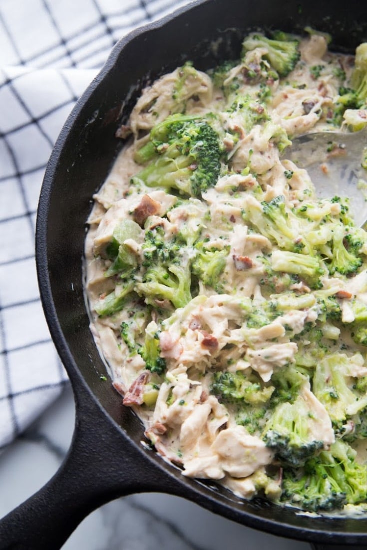 Shredded chicken breasts with broccoli, cheese and cream in a skillet for keto chicken bacon ranch casserole.