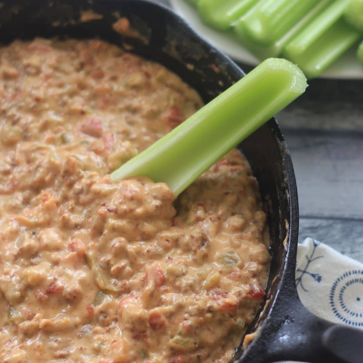 sausage & cheese dip in a cast iron skillet with celery
