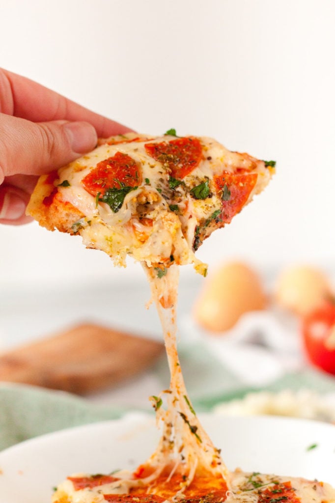 a hand holding a slice of keto pizza