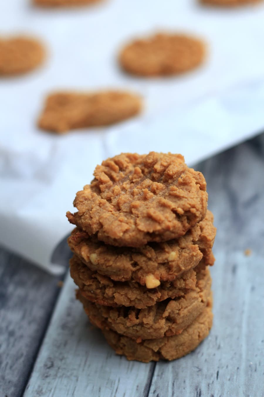 Low carb Peanut Butter cookies stacked five high with a cookie sheet in the background with several cookies on it.