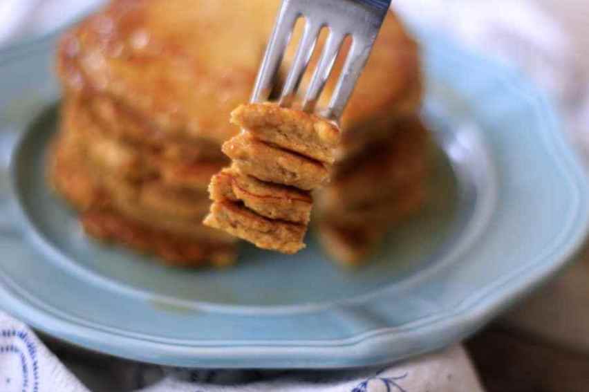 Close-up view of a stack of fluffy pancakes on a light blue plate, with a fork lying in front of the stack after cutting out a wedge-shaped bite from the pancakes.