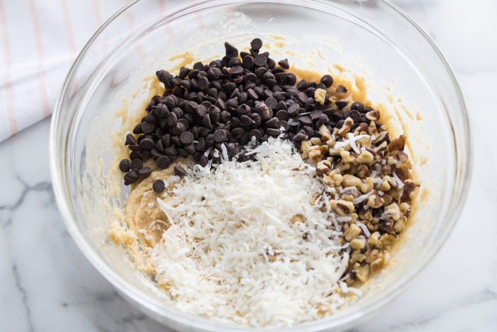 Chocolate chips, walnutes, coconut and batter being mixed together in a bowl