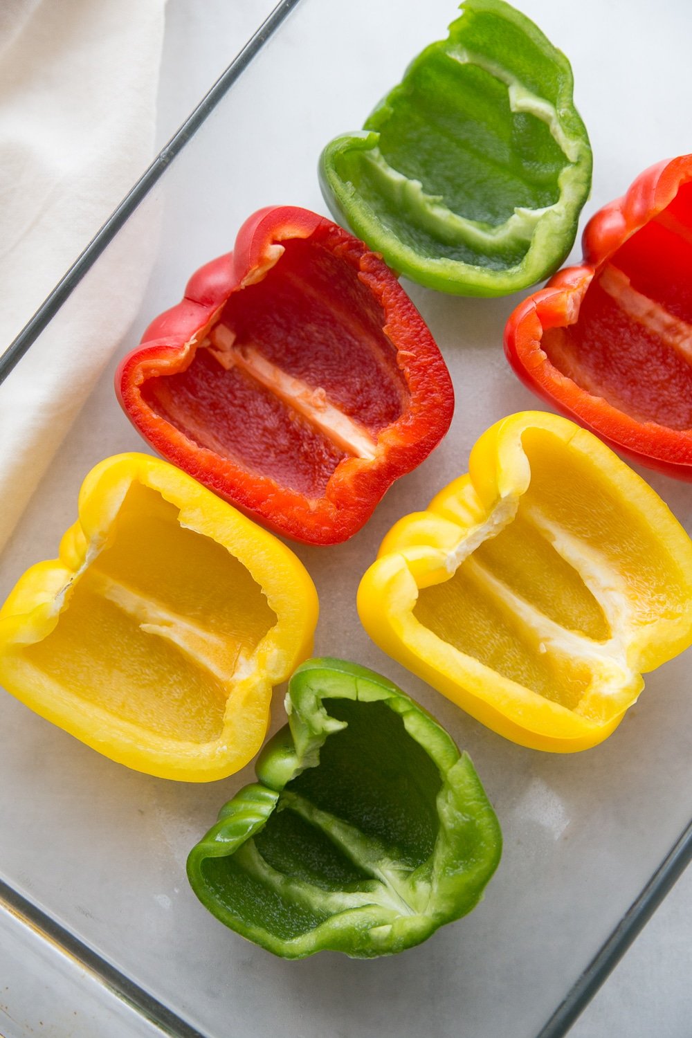 Red, yellow, and green bell peppers that have been halved sitting in a glass pan