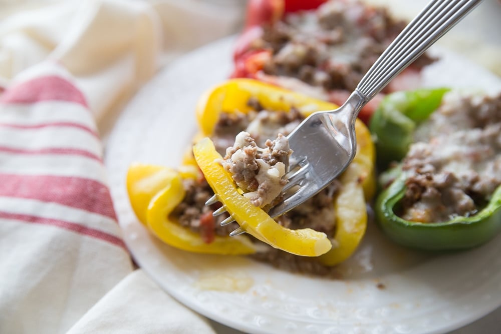 Finished keto stuffed bell peppers on a plate, with a fork with a bite of peppers on it in the front.