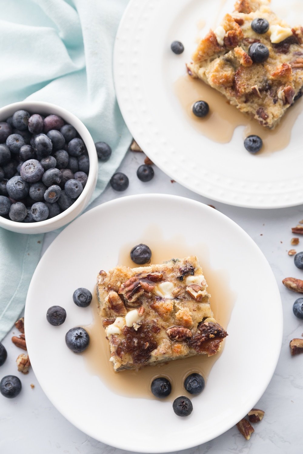 Two plates of french toast casserole with blueberries and maple syrup