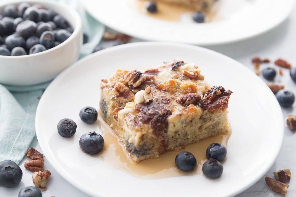 Slice of french toast casserole on a plate with maple syrup and blueberries