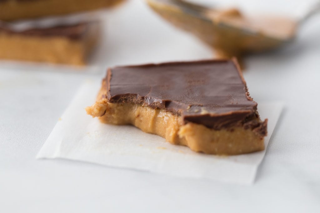 No Bake-Keto Peanut Butter Bars cut in a square with a bite out on a square of parchment paper