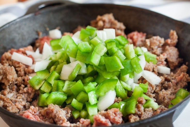 cast iron skillet with browned sausage and chopped onions and green peppers for low carb breakfast casserole
