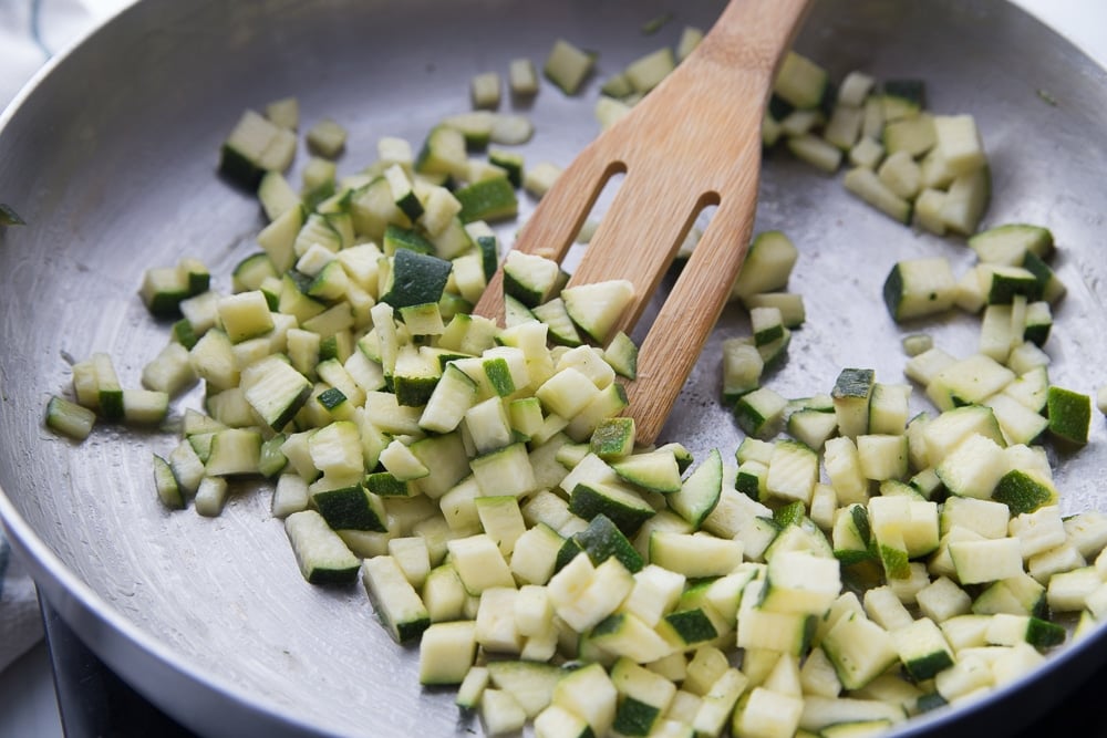 sautéed zucchini in a skillet with a wooden spoon