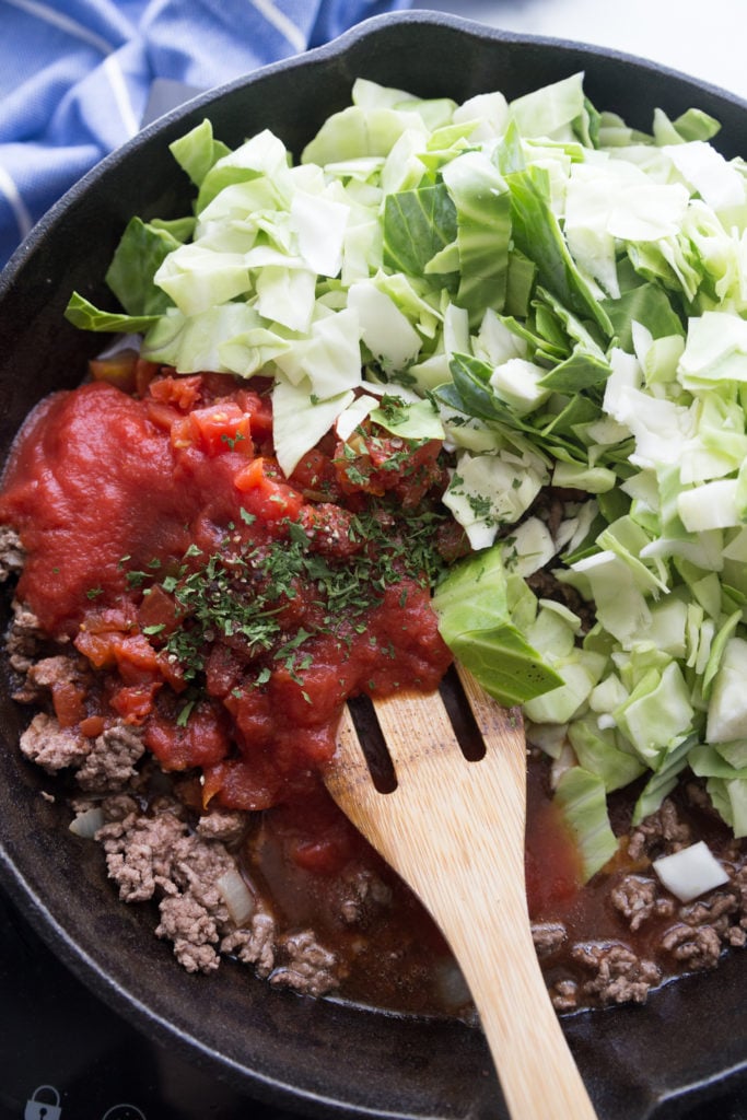 Cast iron skillet of ground beef, tomato sauce, parsley and cabbage before cooking