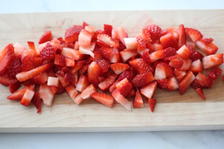 Strawberries chopped on a wooden cutting board.