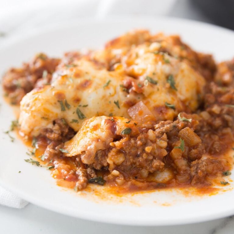 Cheesy Italian keto beef skillet served on a white plate with melted mozzarella, seasoned ground beef, marinara sauce, and fresh herbs.