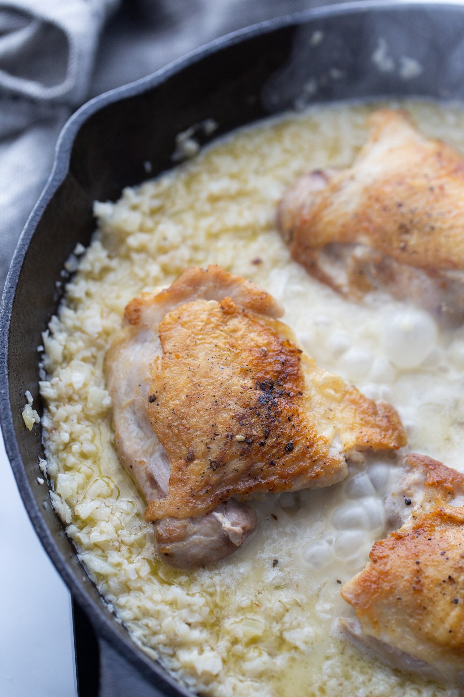 boiling chicken thighs and riced cauliflower in a cast iron pan