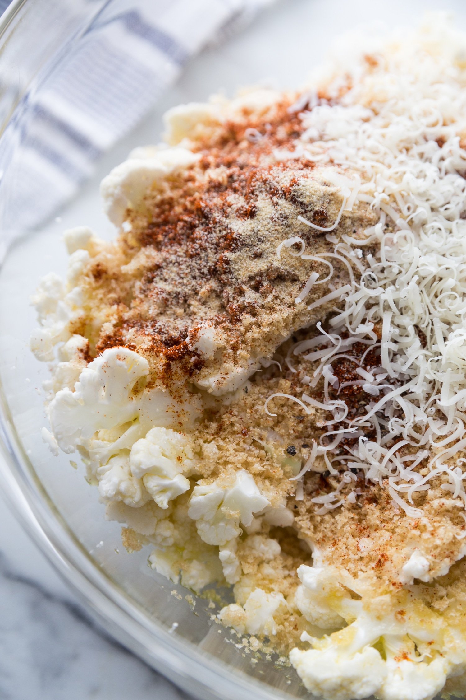 Cauliflower florets being mixed with pork panco bread crumbs, olive oil, parmesan cheese, and spices.