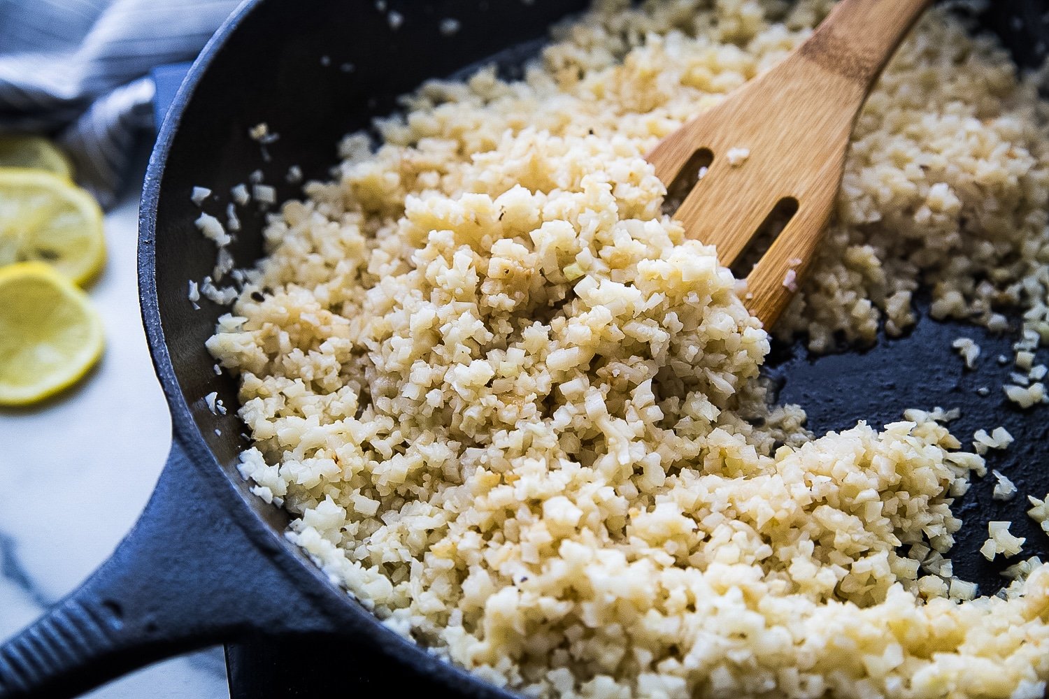 Riced cauliflower being fried in butter in a cast iron skillet.