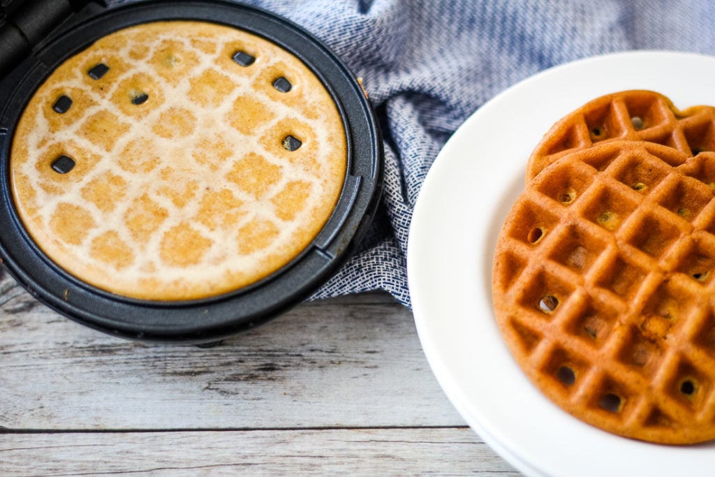 pumpkin Chaffle batter in the mini dash waffle maker with a keto waffle sitting next to it.