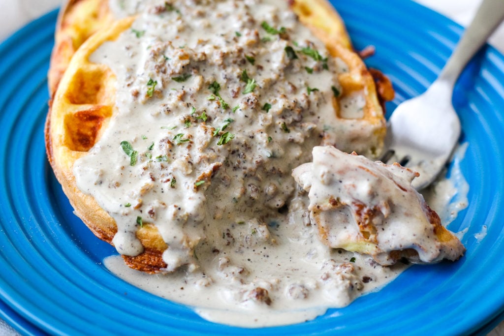 chaffle with keto sausage gravy plated on a blue plate with a bite on a spoon