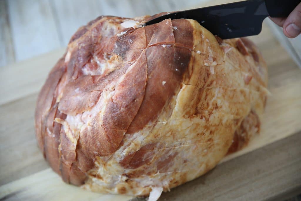 scoring a bone-in ham with a knife on a cutting board