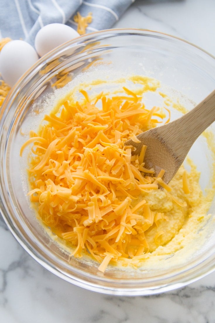 An image of a bowl with biscuit batter and shredded cheese with a wooden spoon.