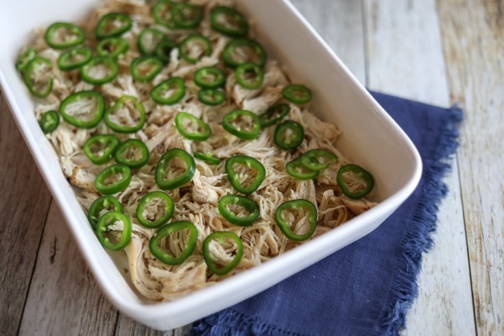 shredded chicken in a white casserole dish topped with sliced jalapenos