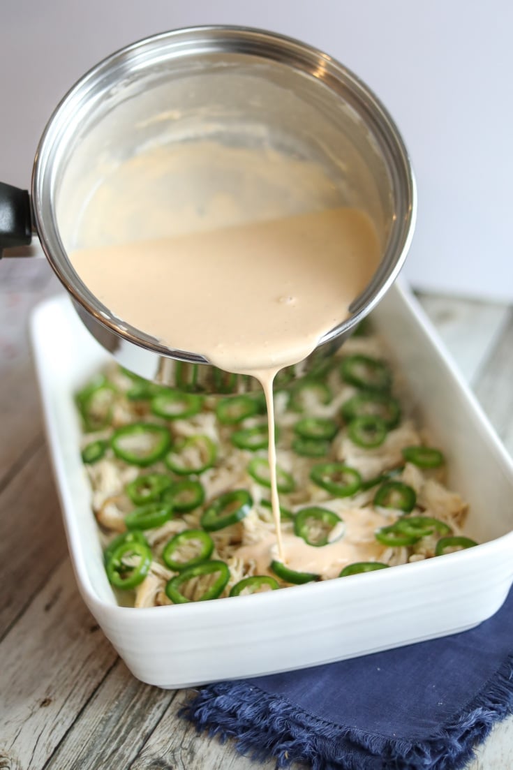 white cream sauce being poured over top of the chicken and jalapenos