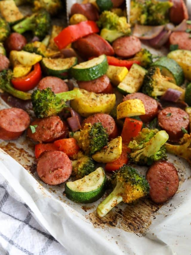 Overhead view of sheet pan dinner with slices of smoked sausage links nestled around broccoli, red bell peppers, purple onions, squash, and zucchini veggies that have been drizzled in oil and seasoning then oven roasted