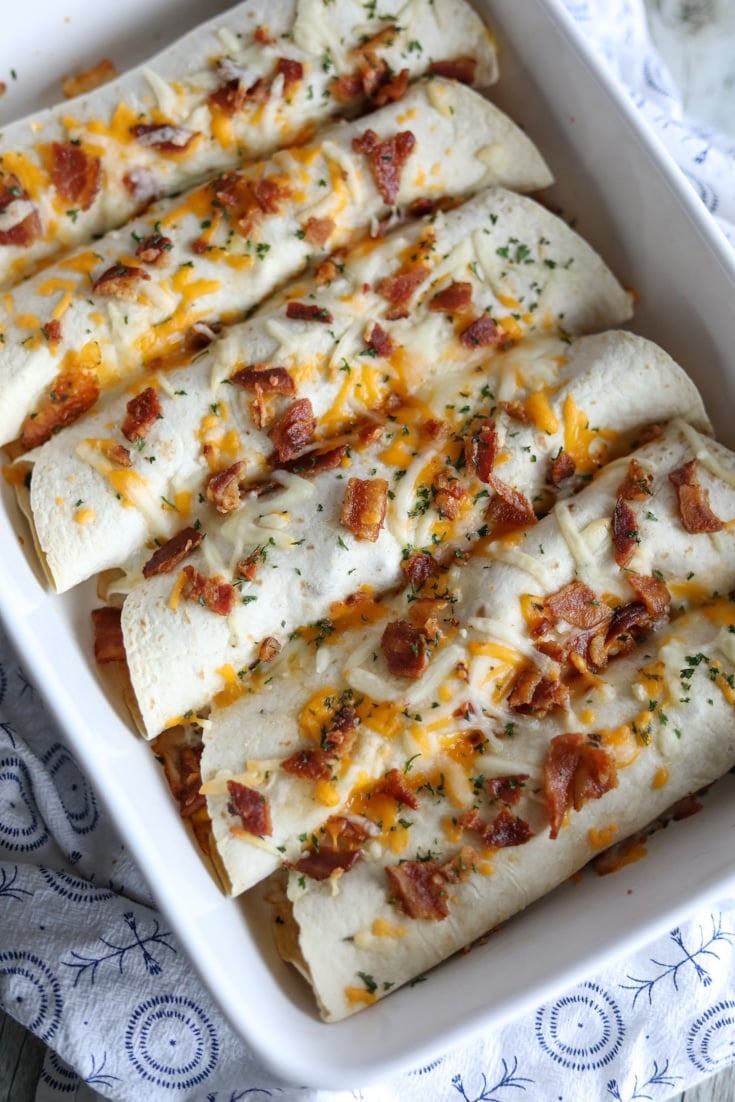 A casserole dish with 6 burritos topped with cheese and bacon.