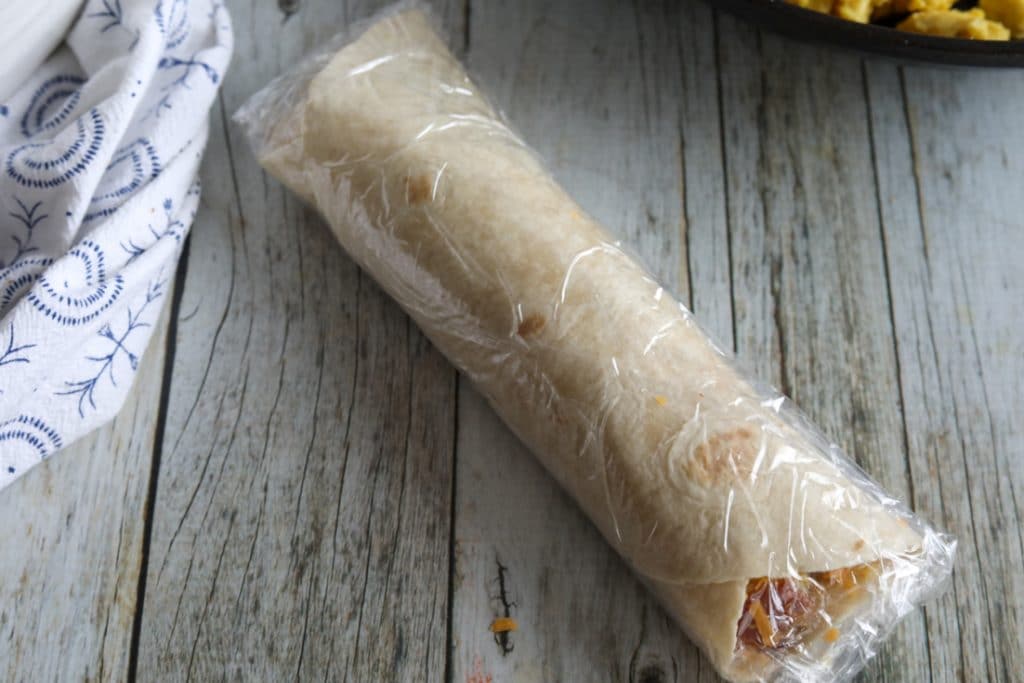 One egg, bacon and cheese burrito wrapped in plastic wrap.