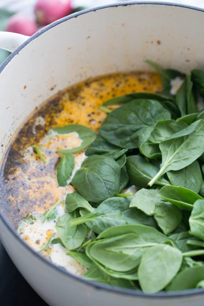 fresh spinach being added to tuscan soup
