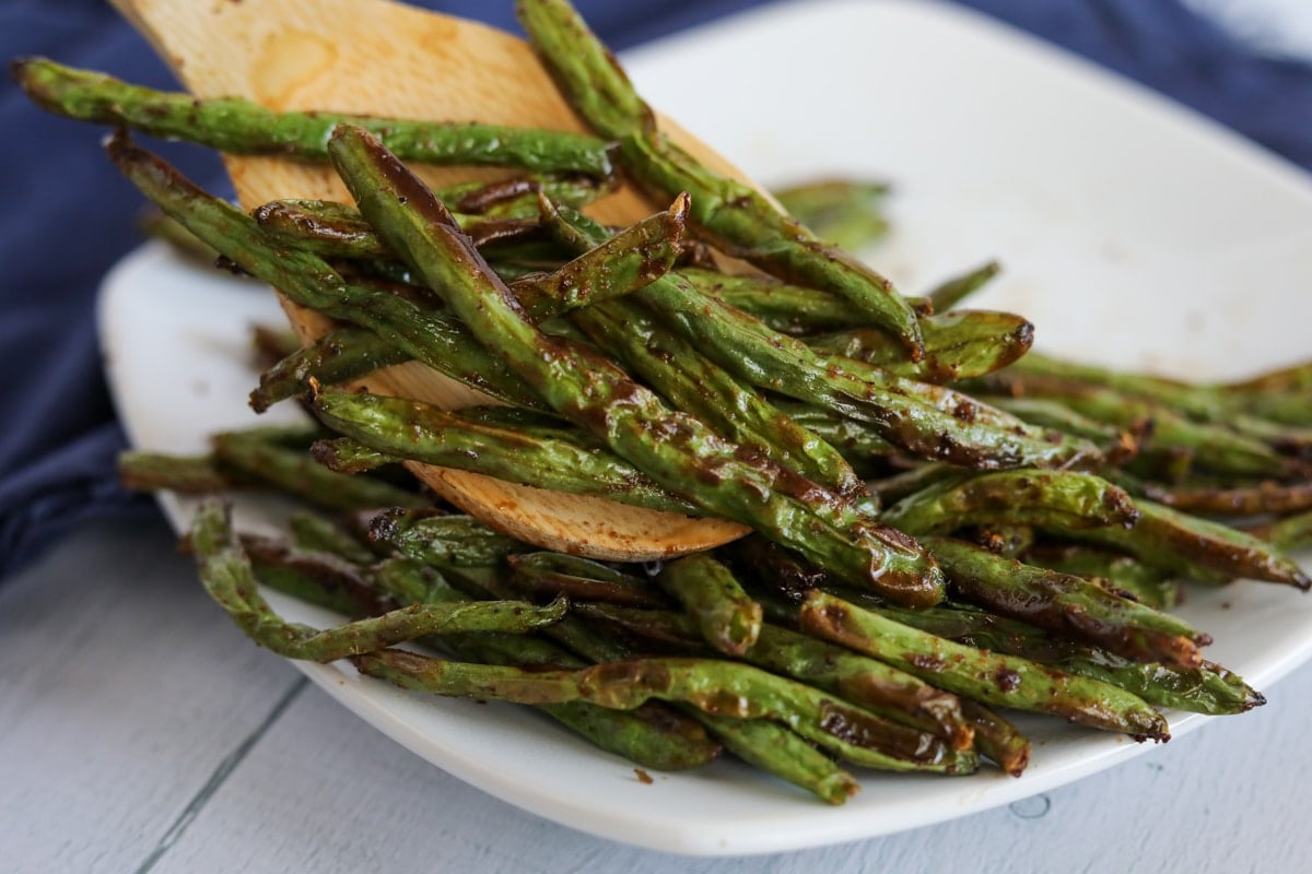Roasted green beans on a plate with a wooden spatula.