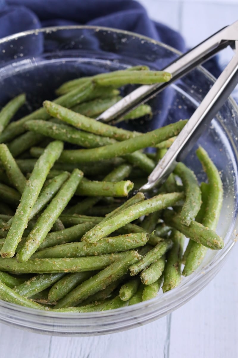 Green beans coated with seasonings in a clear gladdest bowl