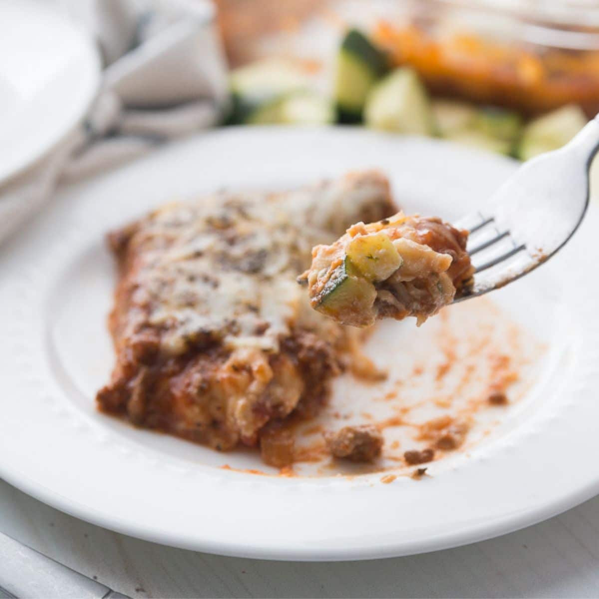 featured image of a serving of keto lasagna on a white plate with a bit on a fork close up
