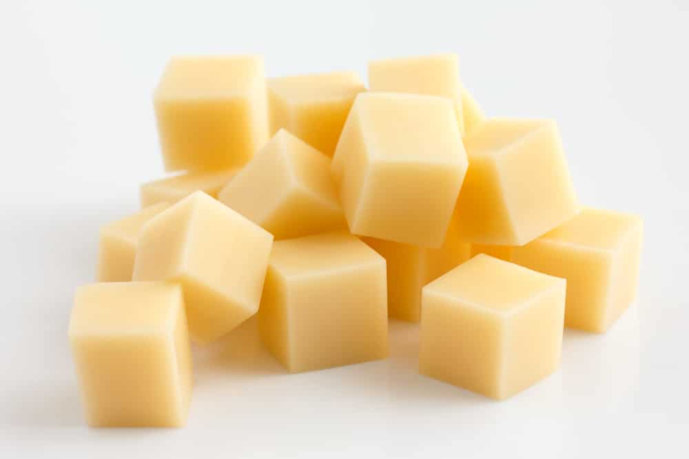 Cubes of yellow cheese stacked randomly on white.