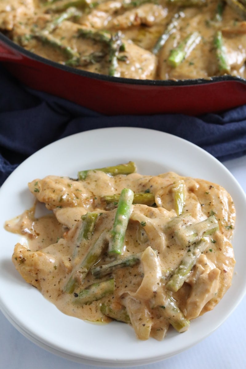 chicken and asparagus in a creamy sauce plated with the skillet in the background