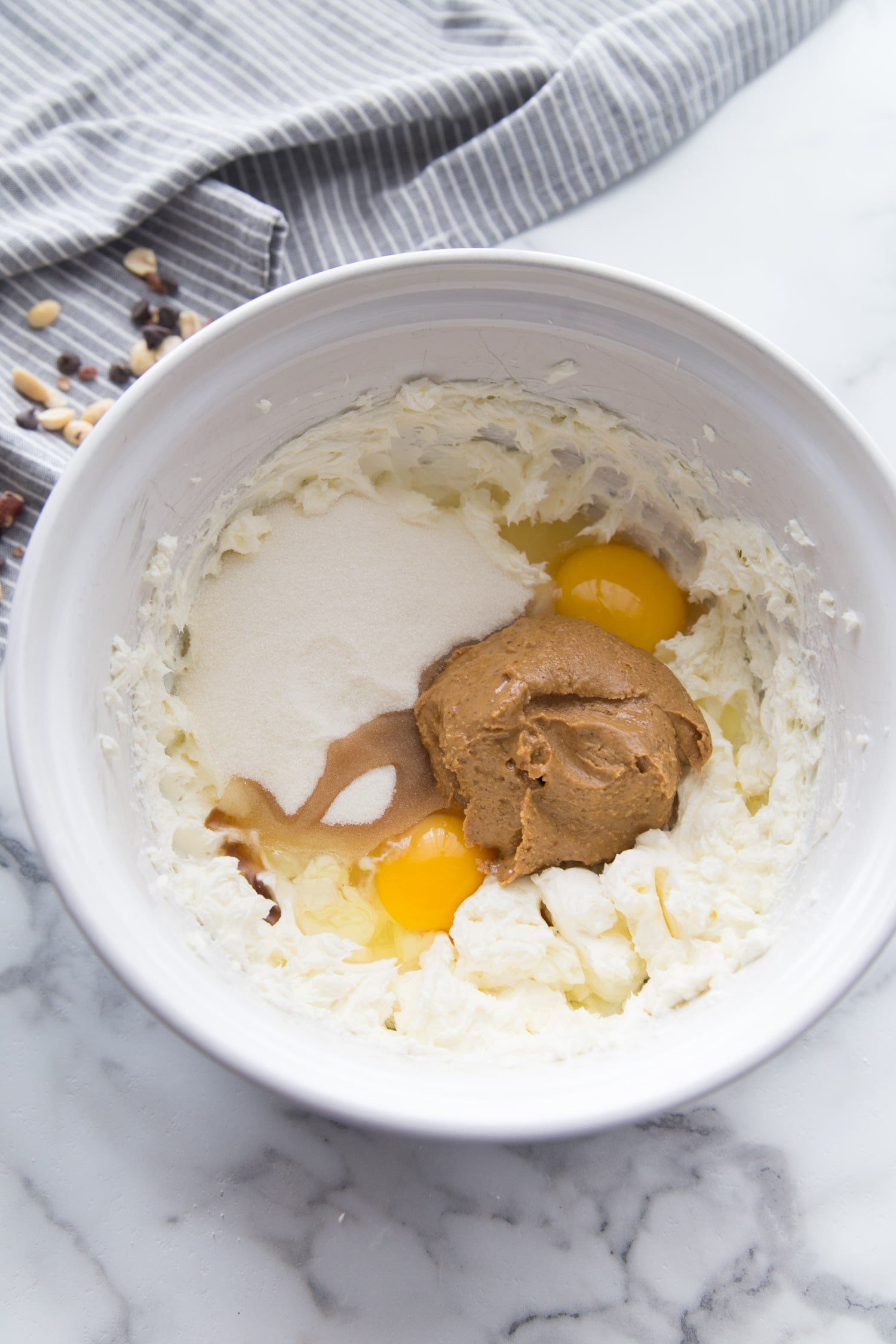 peanut butter, eggs, butter, cream cheese and sugar in a white bowl on marble table