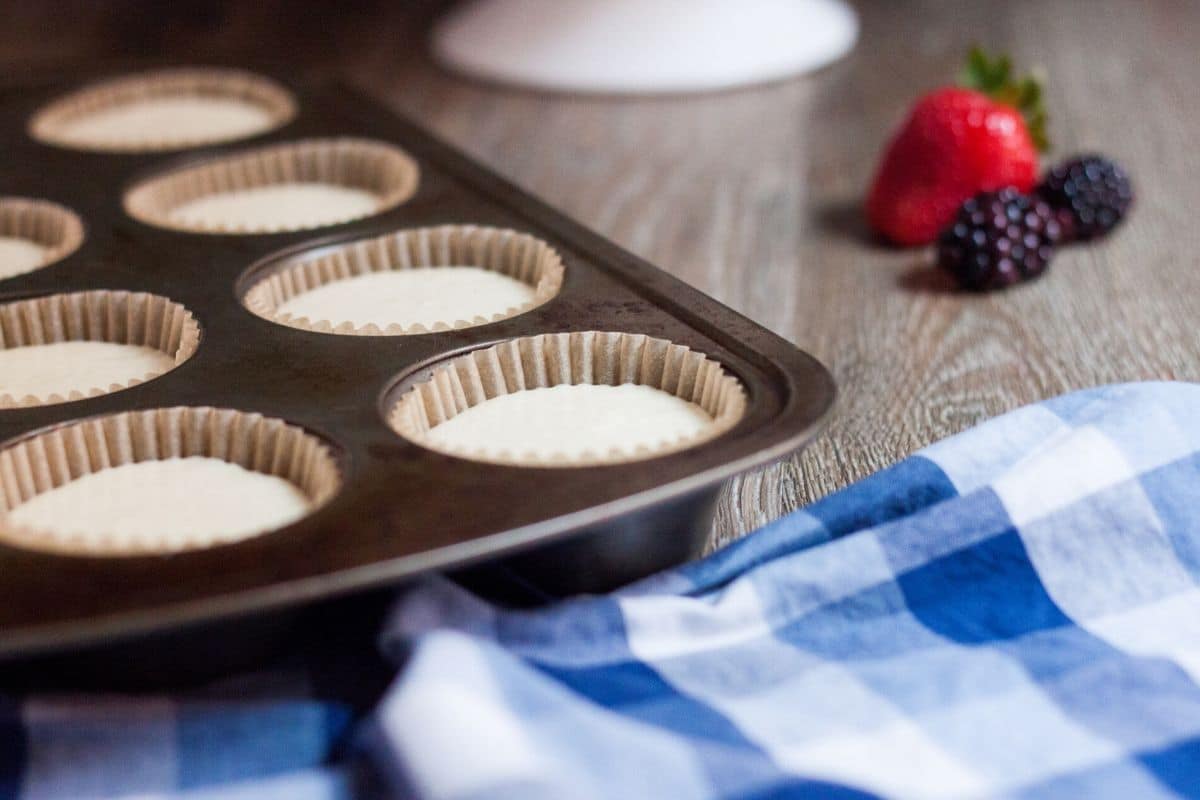 cheesecake batter in a muffin tin with fresh fruit in background